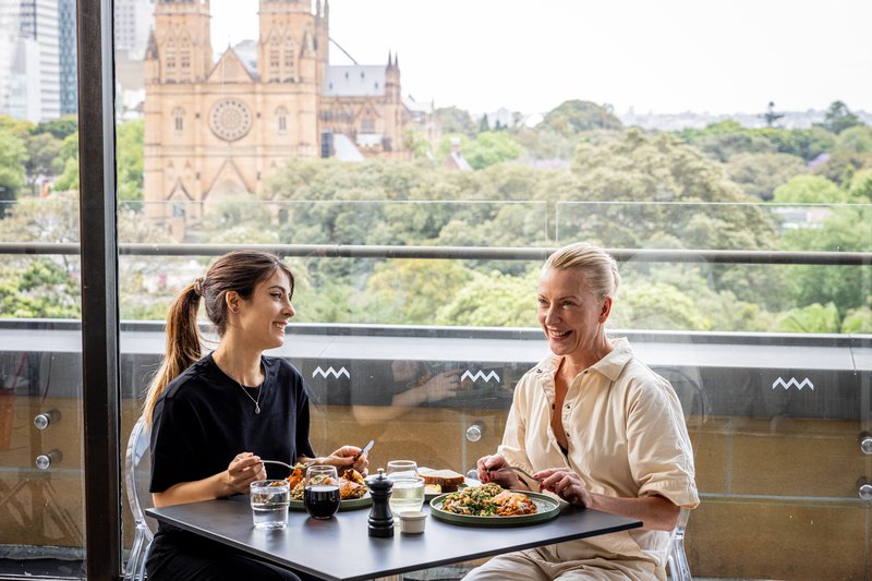 Two women dining at Bistro Gadi with views of St Mary's Cathedral and Hyde Park in background.
