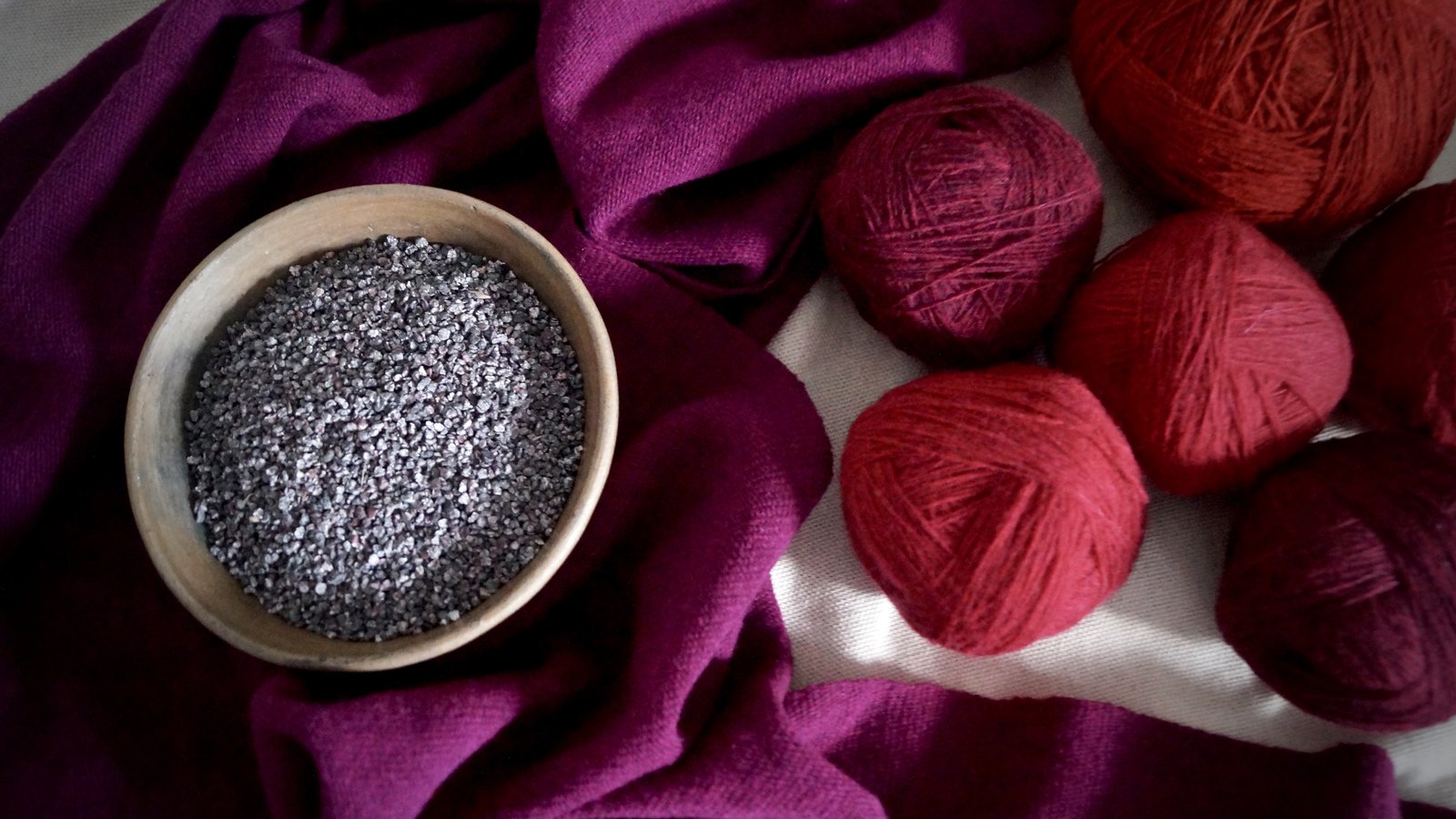 Dried cochineal in a wooden bowl beside red wool yarn balls on purple-dyed fabric, Veracruz, Mexico