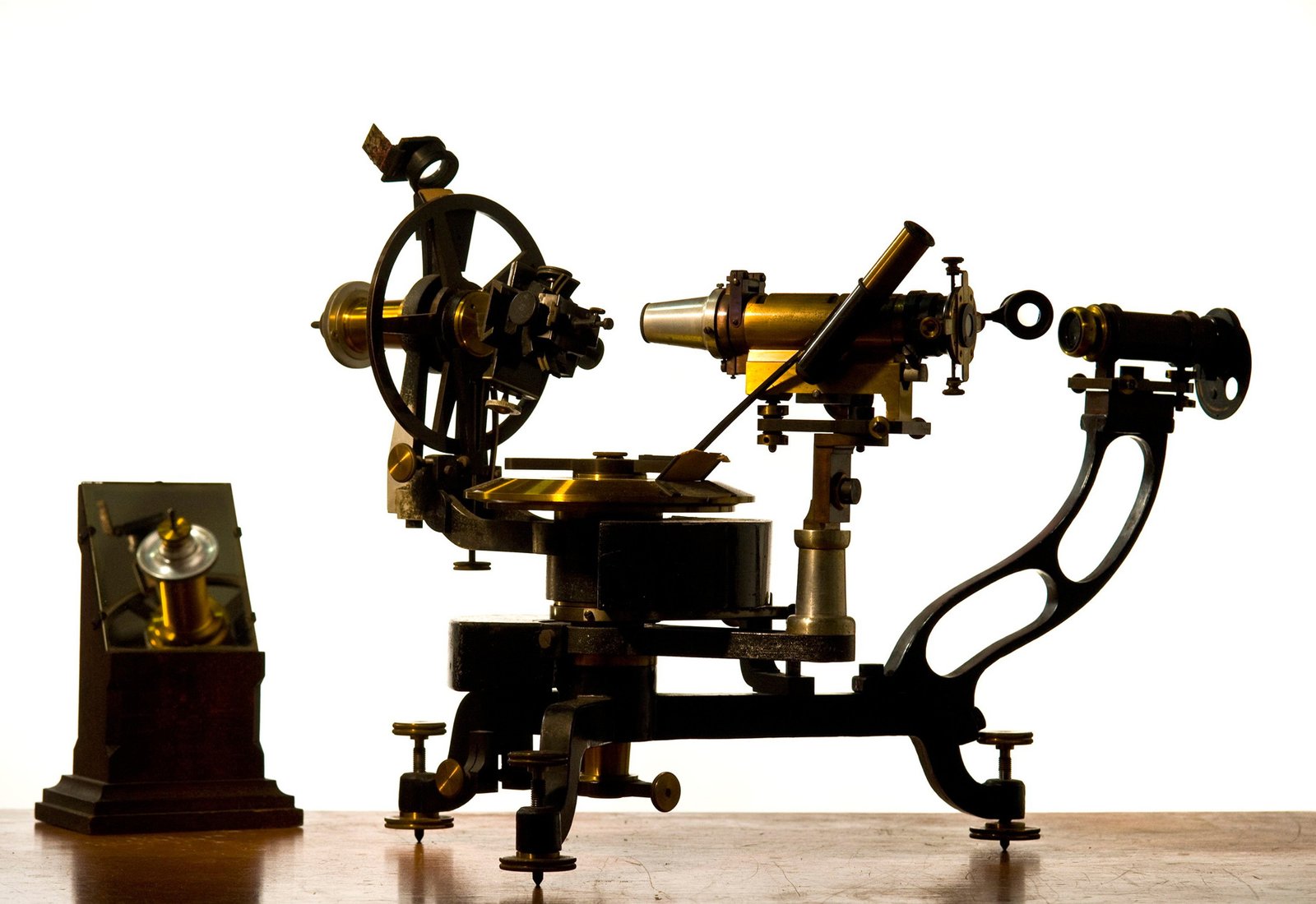 A brass and cast iron two-circle reflecting goniometer on a wooden surface on a white background.