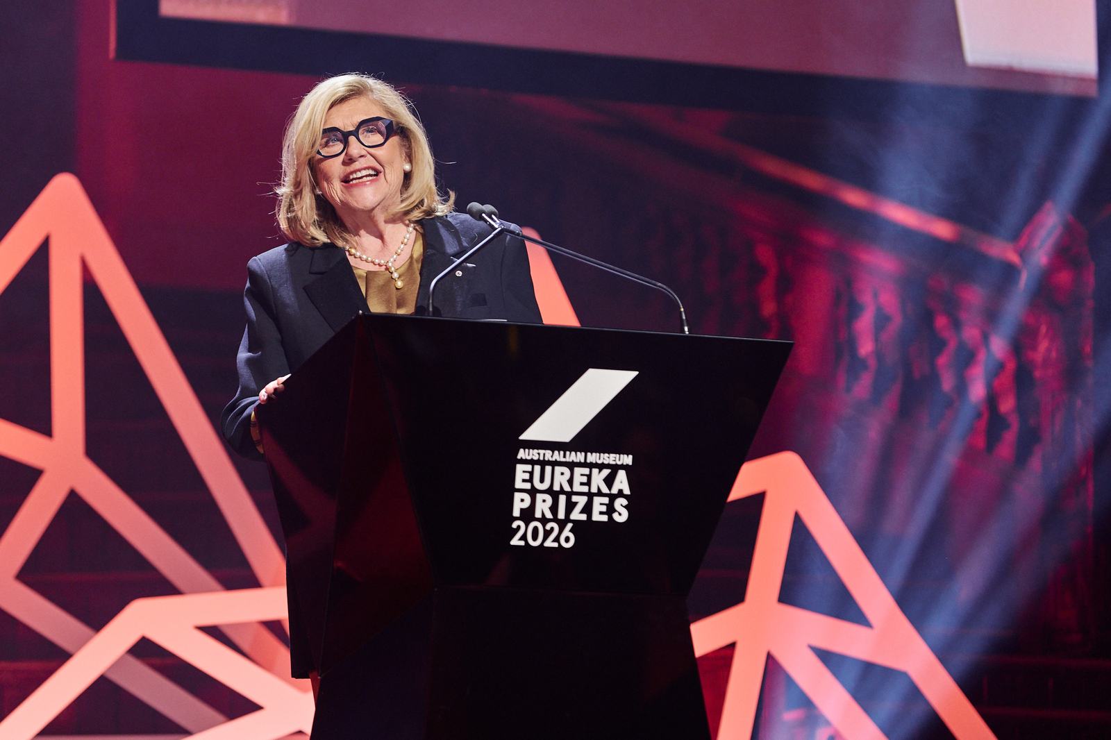 Kim McKay is giving a speech on stage with a microphone at the Eureka Prizes 2026.
