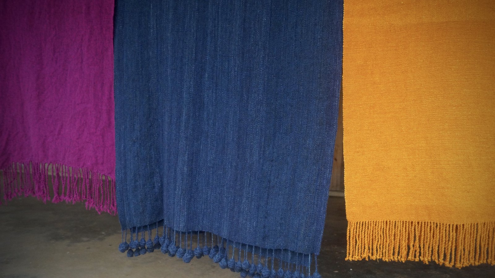 Three handwoven shawls in purple, blue, and yellow hanging side by side, Tlaquilpa, Veracruz.