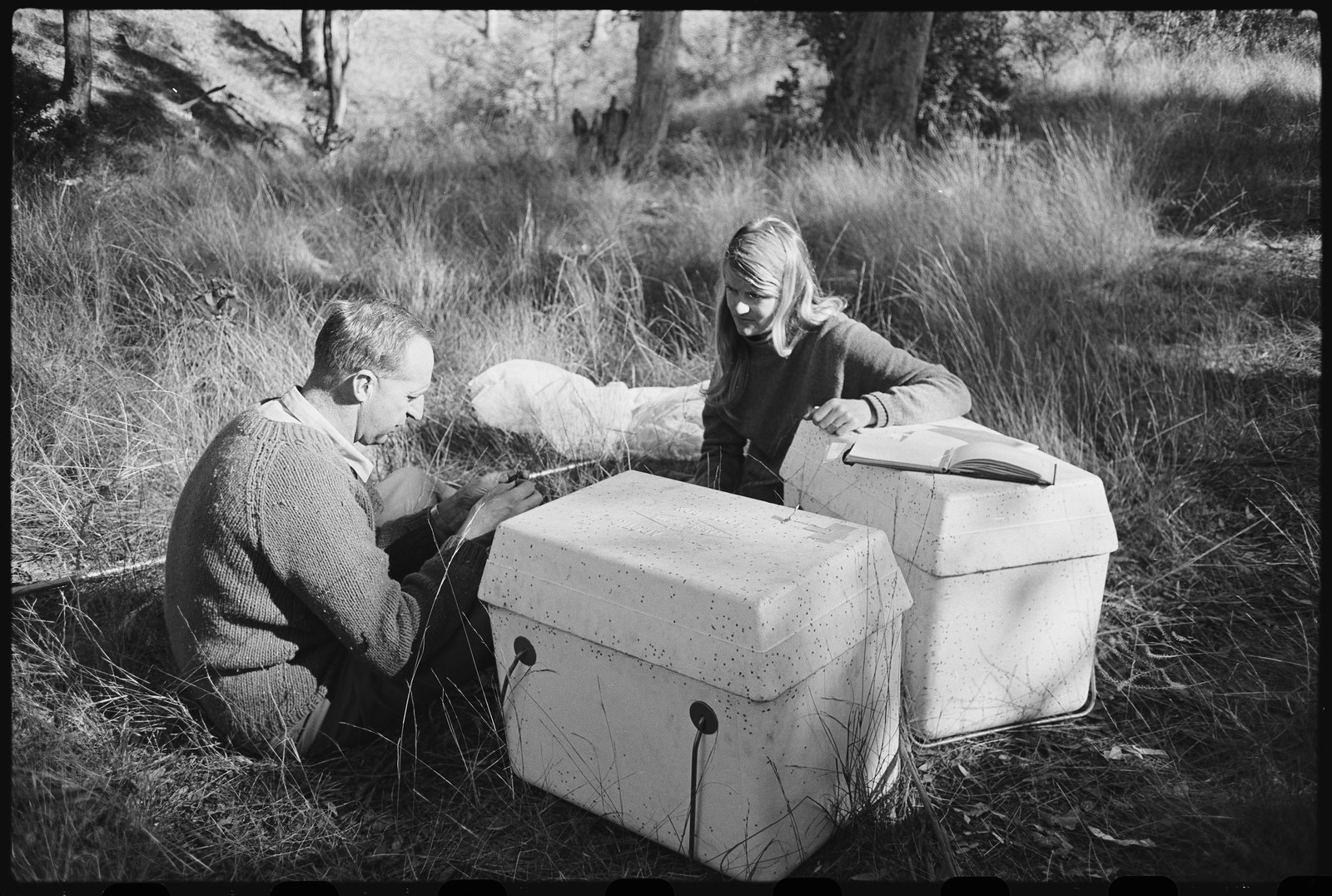 Black and white photograph of a man and a woman with two white boxes, in a field.