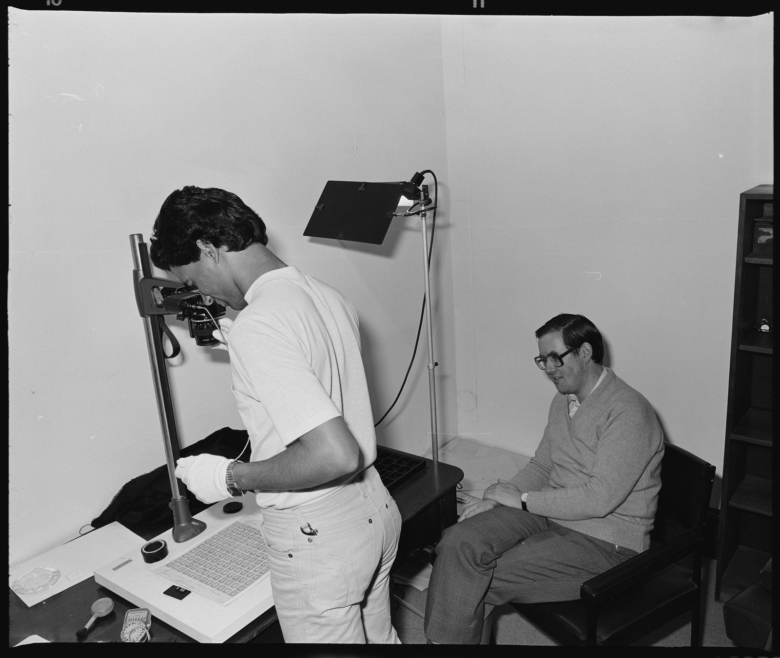 Black and white photograph of two men taking images of stamps with various pieces of equipment.