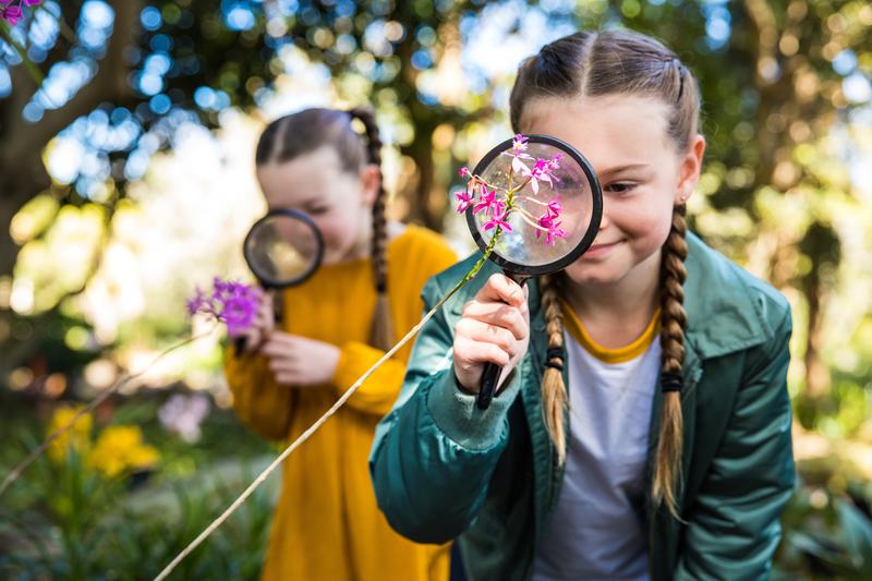 Two girls looking at flowers through magnifying glasses