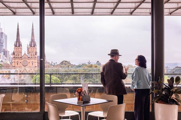 Two people standing in the Bistro Gadi restaurant looking out the window at the city view.