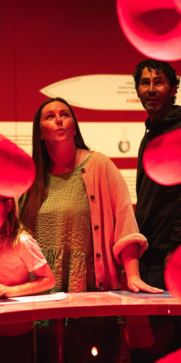Two children and two adults look up in wonder at giant red blood cell models in Bloodsuckers.