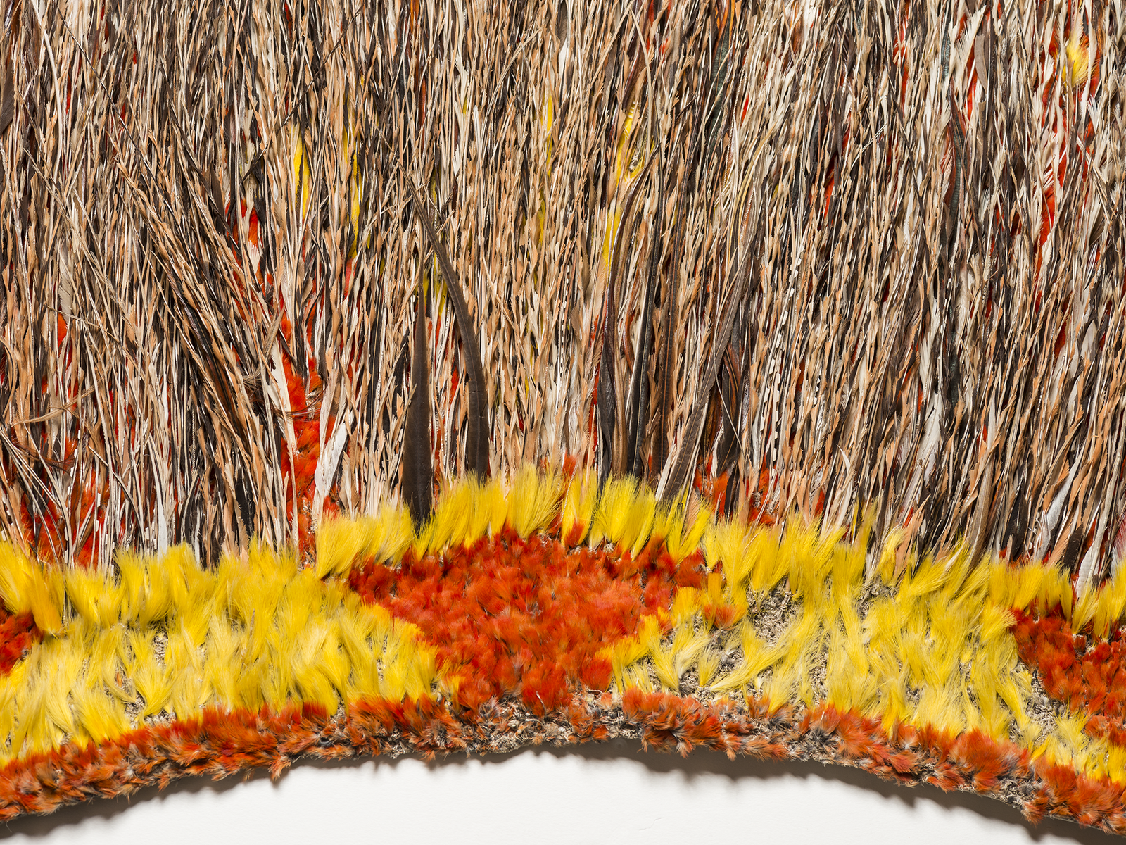 Detail of a Hawaiian feather cape showing densely layered red, orange and yellow feathers.