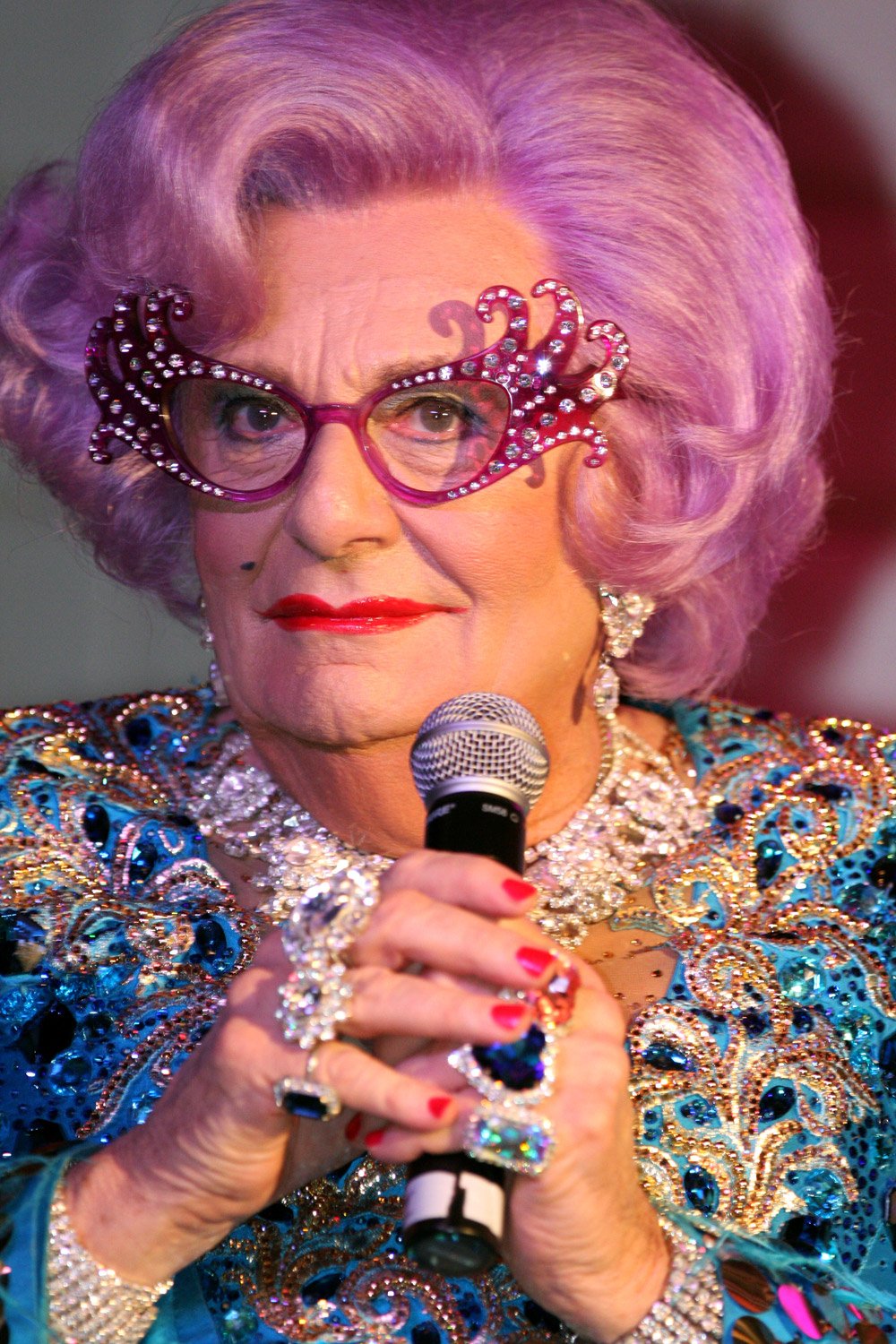 Performer Dame Edna Everage holding microphone wearing iconic glasses and sparkling dress