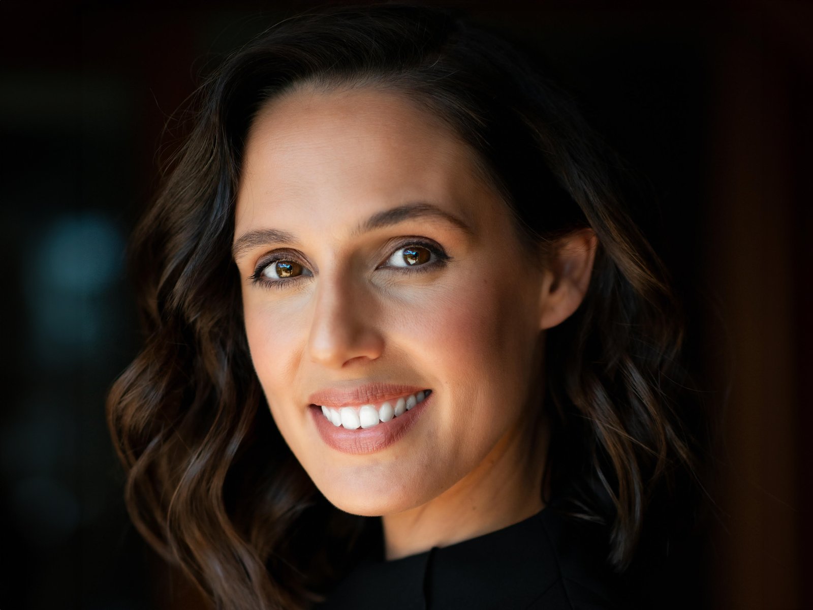 Close-up portrait of a smiling woman with dark wavy hair wearing a black blouse.