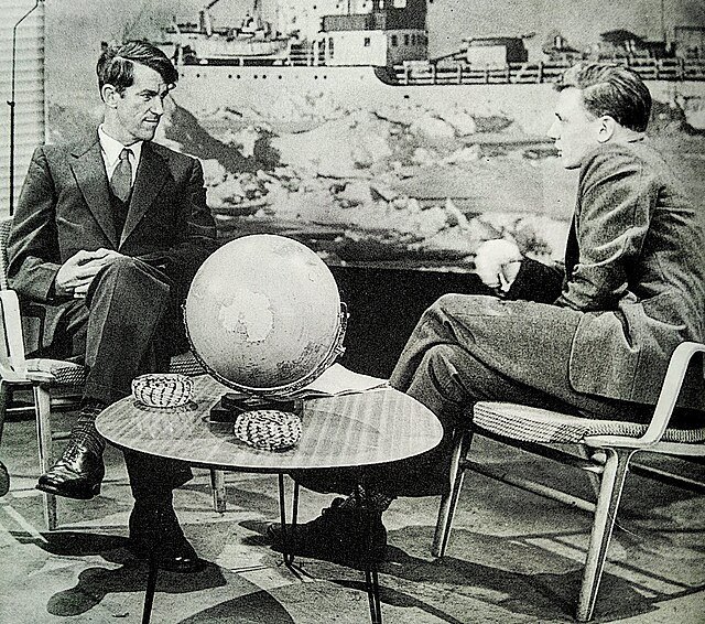 Black and white photograph of two men sitting in chairs, behind a table with a globe.