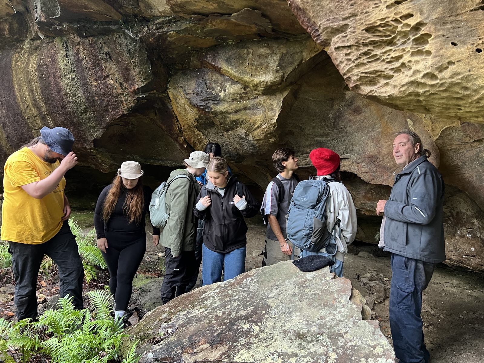 Students and a guide examining a rock shelter site identified through drone surveying in the Blue Mountains.