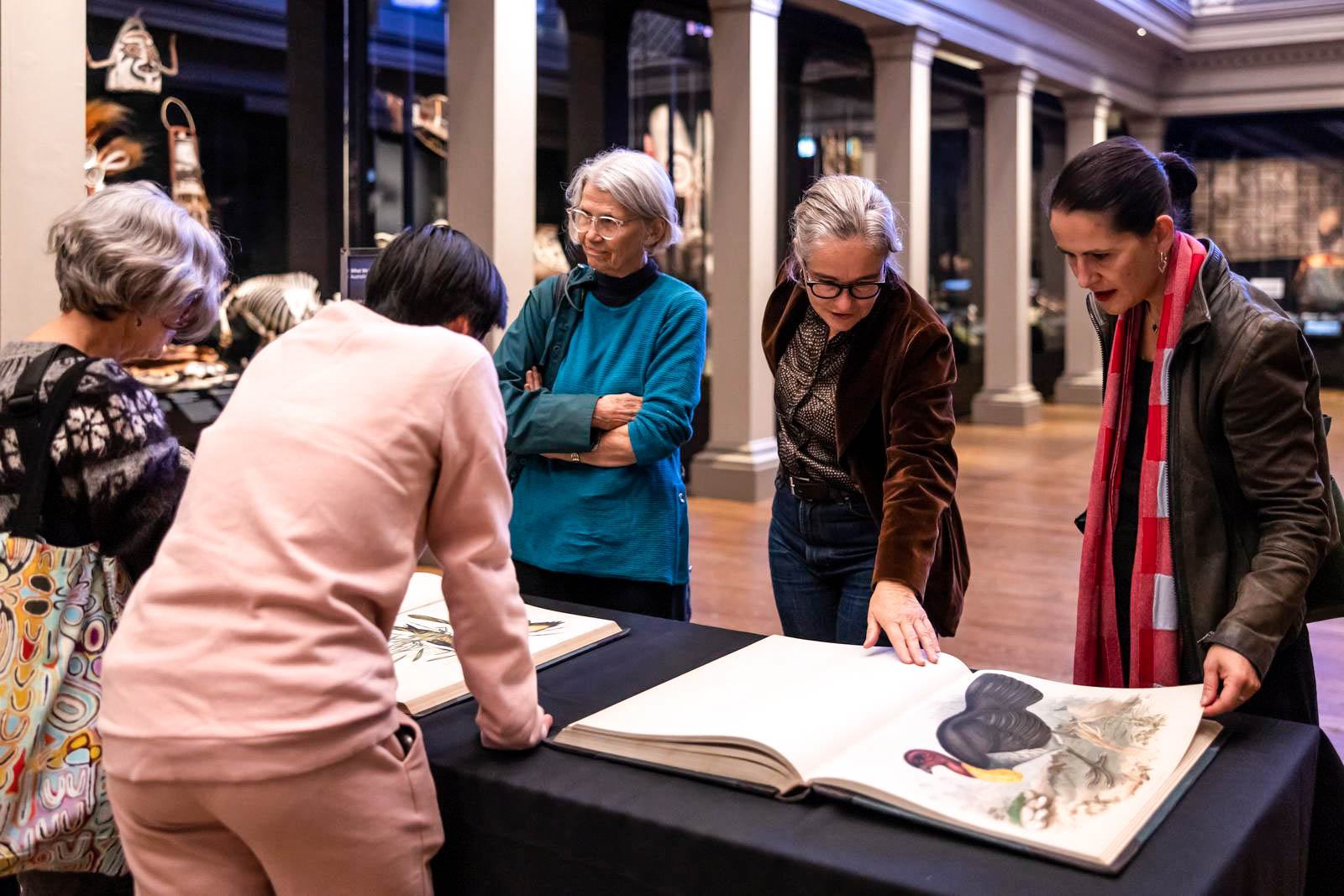 A group of people are gathered around a table with an open rare book in the Australian Museum.