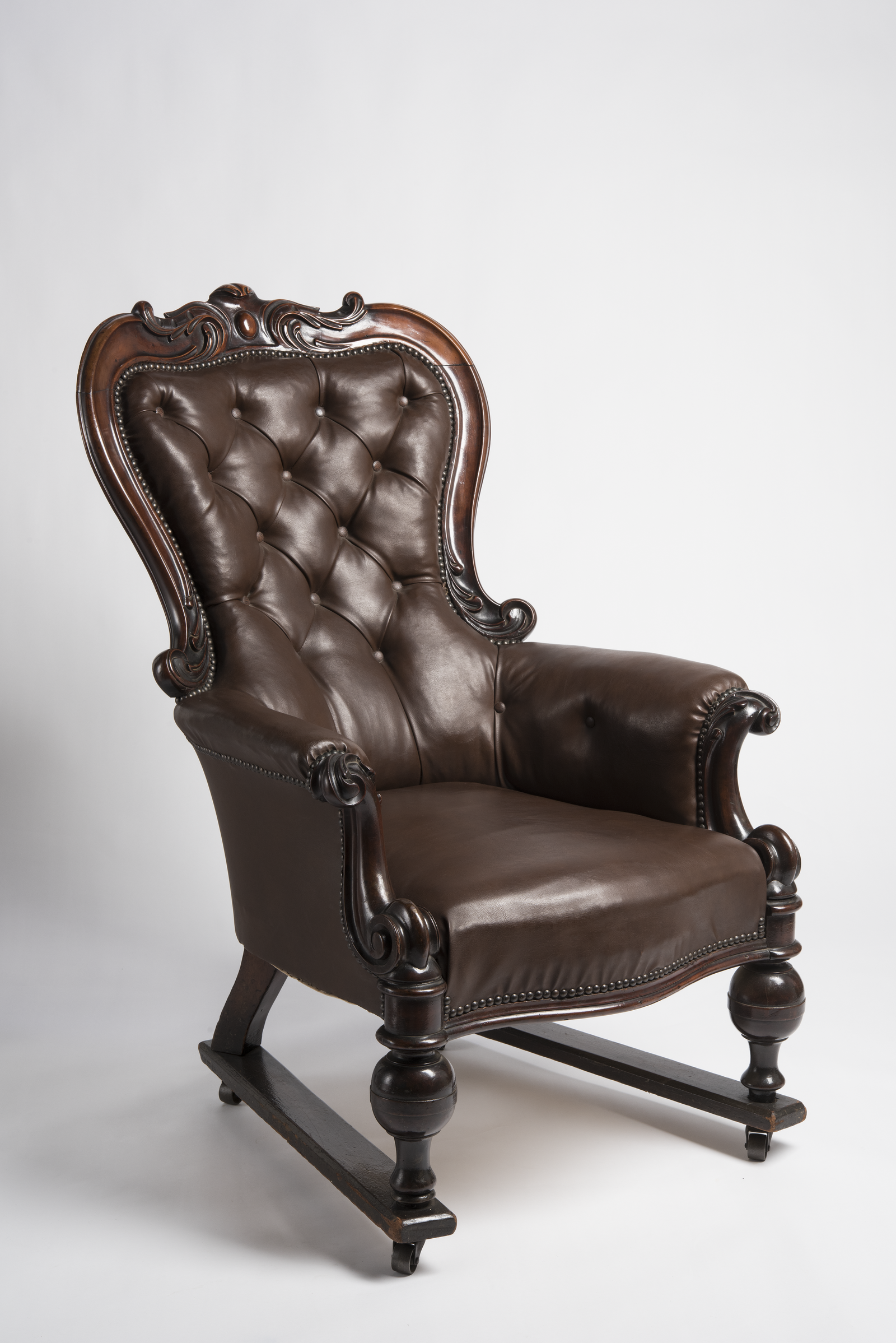 Victorian button-tufted leather armchair with carved cedar frame and scrolled detailing on castors