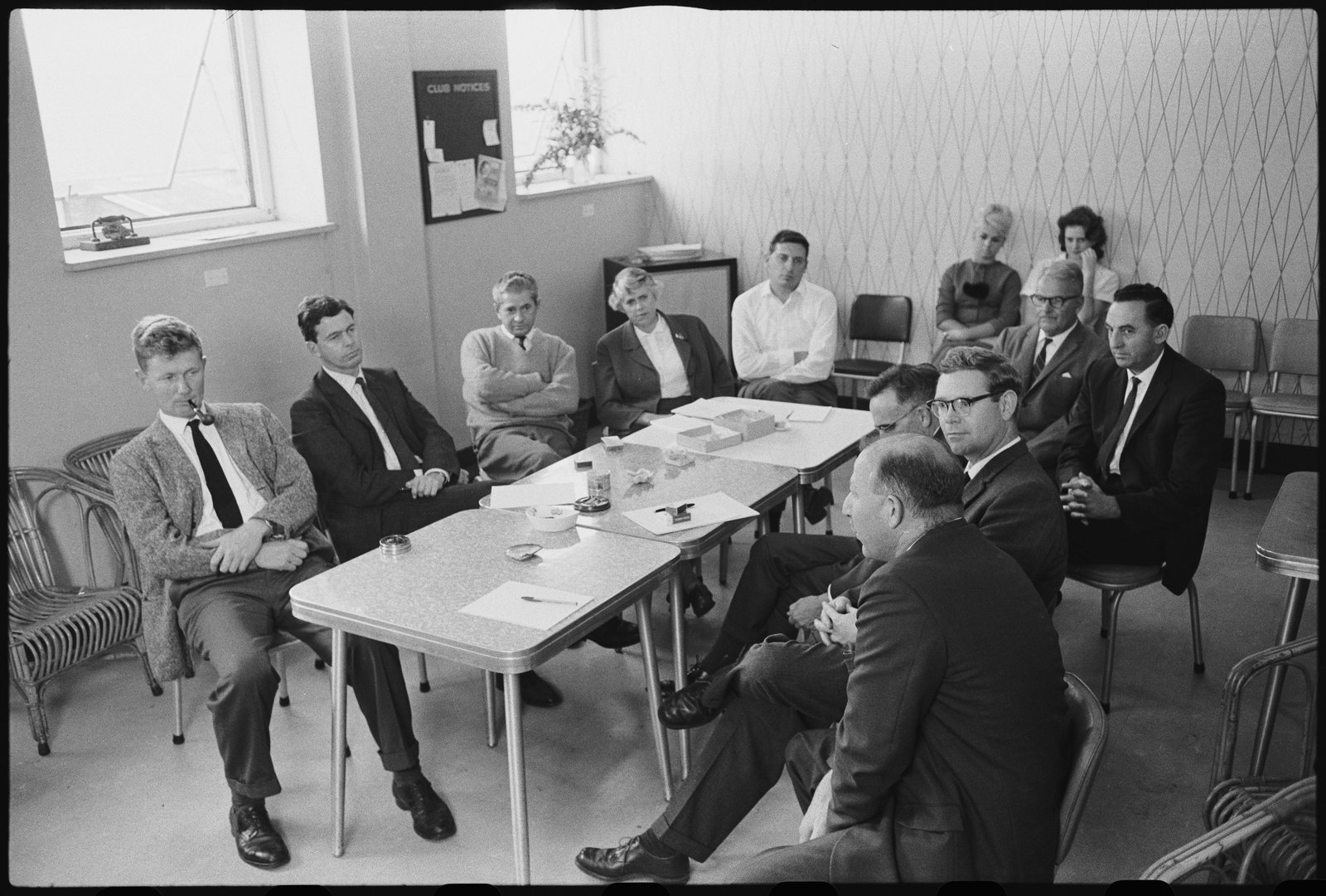 Black and white photograph of a group of men and some women at a table in a meeting room.