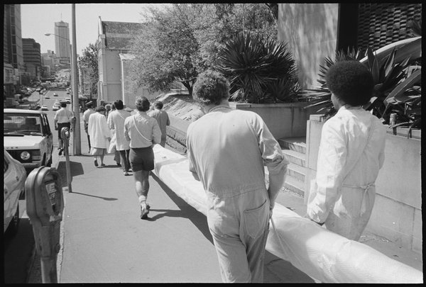 M02774_23 [Australian Museum staff carrying large pole, possibly a Pasifika cultural collection object, out of the Museum building, down William Street]