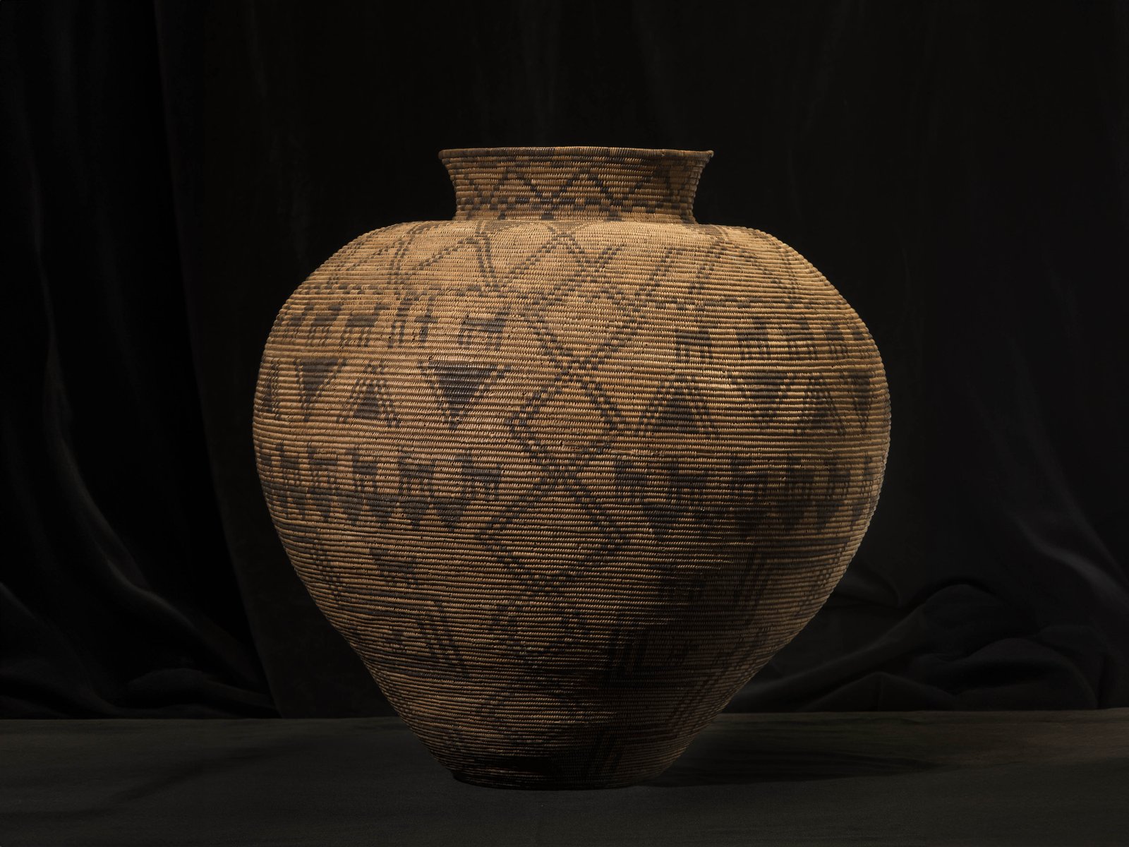 A large round coiled basket with a narrow neck decorated with geometric and animal motifs