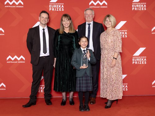 Teacher with parents and student holding trophy on red Eureka Prizes media wall background.