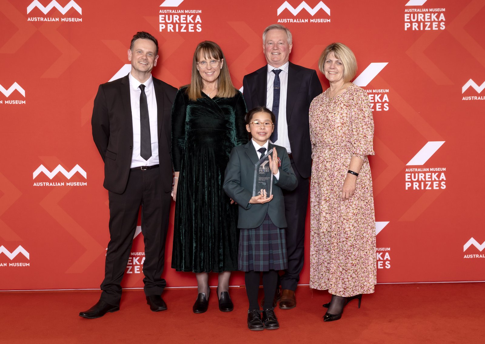 Teacher with parents and student holding trophy on red Eureka Prizes media wall background.