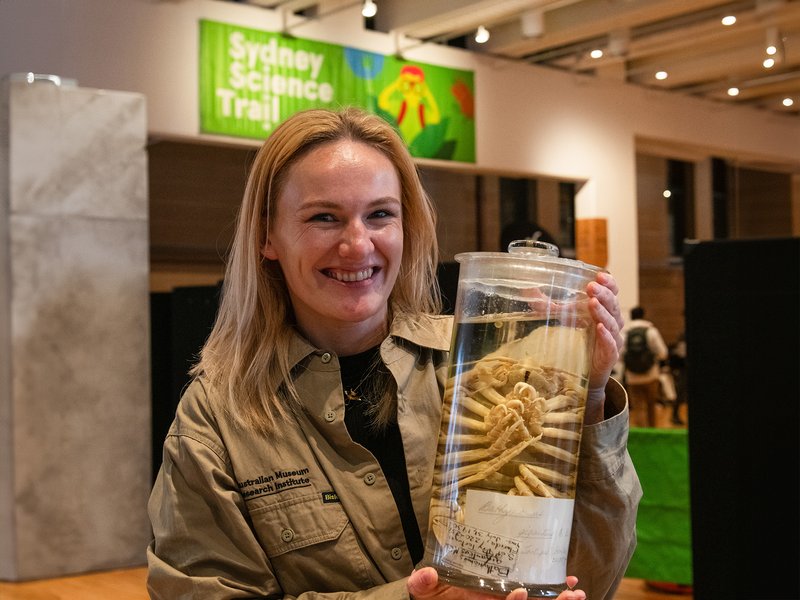A smiling woman holds a large clear jar containing a preserved specimen at the Sydney Science Trail