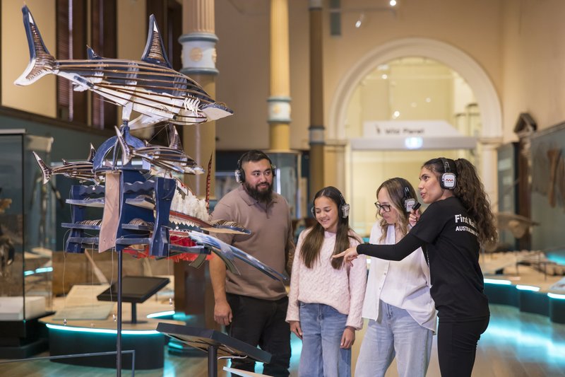 A First Nations guide leads a family wearing headphones in Garrigarrang exhibition.