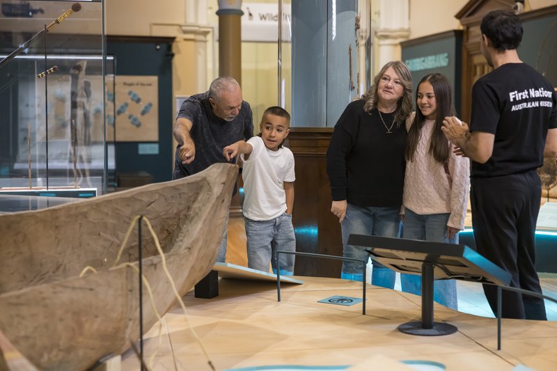 A First Nations guide shows a family a large wooden canoe in the Garrigarrang Sea Country exhibition