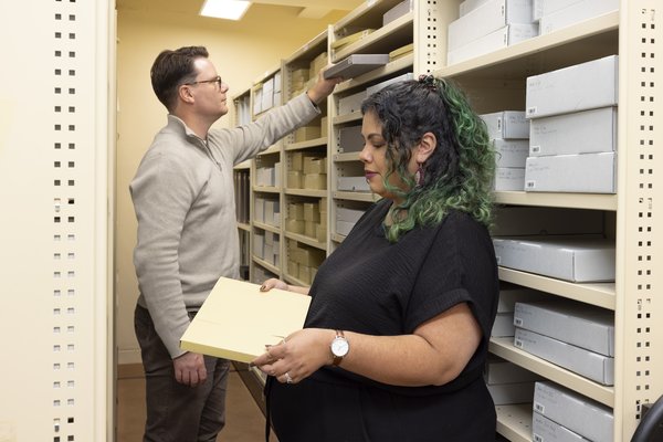 Two people retrieve archival boxes from shelving in a museum collections room.