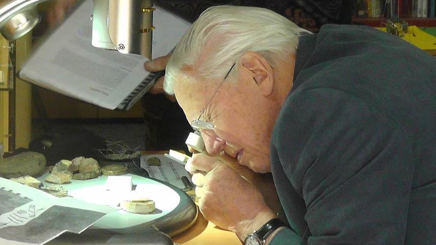 Older man using a magnifying glass to look at a fossil under a microscope.