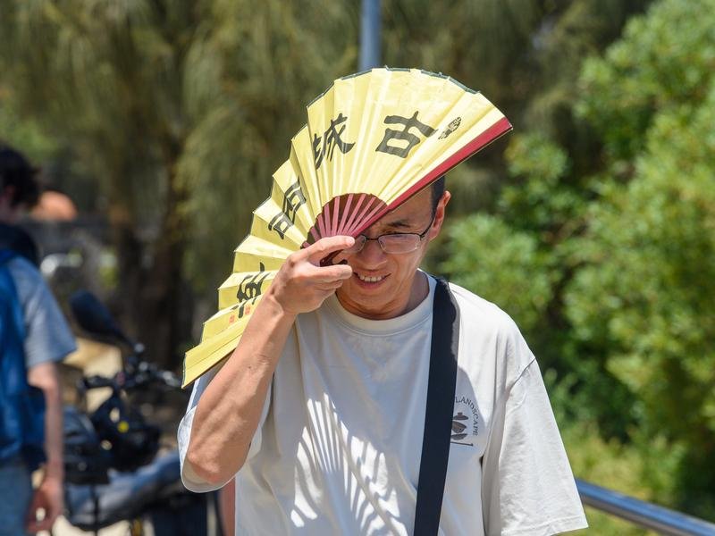 A man shades himself from the heat with a fan