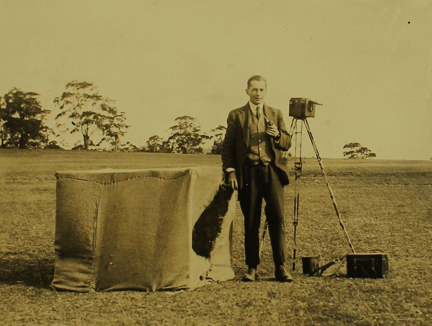 Yellowed black and white photograph of a man with a bird hide and camera.